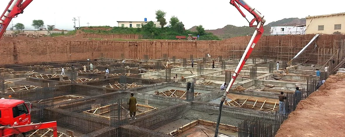 Industrial building foundation construction with heavy machinery and concrete work in progress